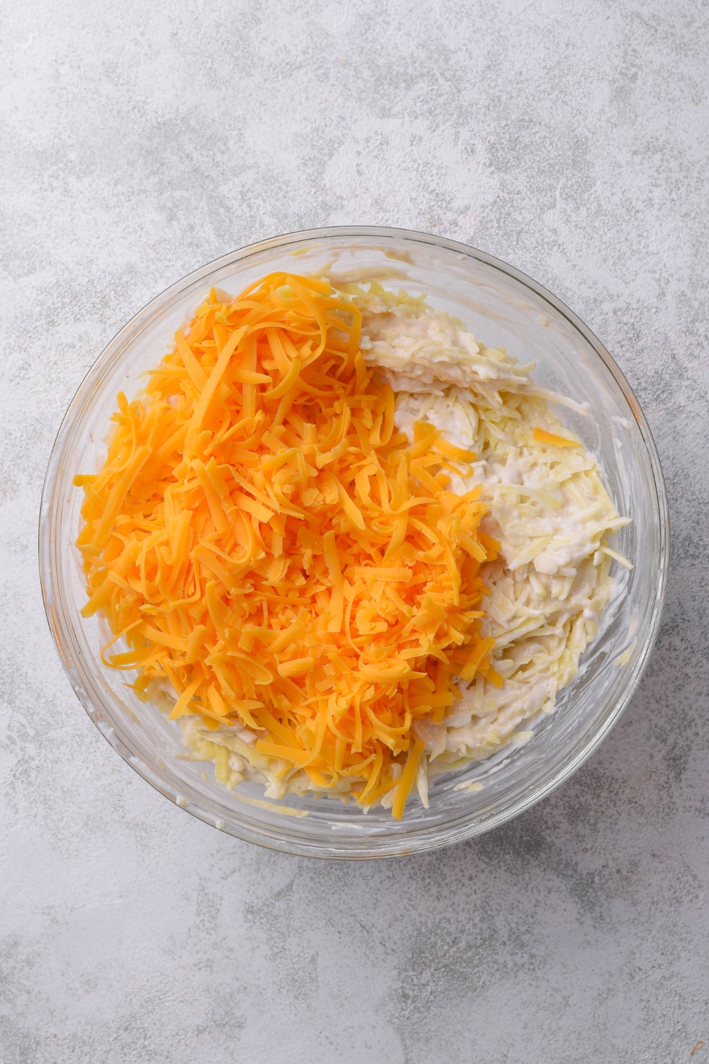 A mixing bowl with the hashbrown mixture and the shredded cheese added to it.
