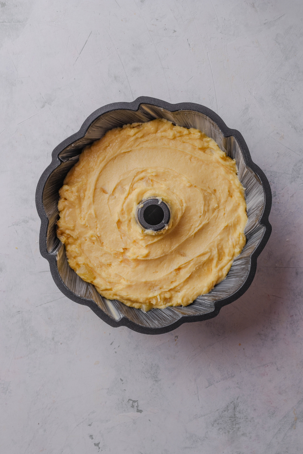 A black bundt cake pan holds pineapple pound cake batter ready to be baked.