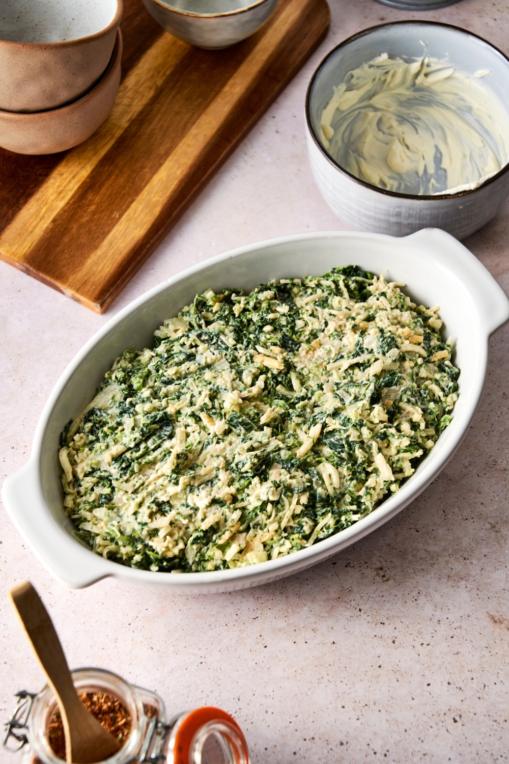 A casserole dish with unbaked spinach dip in it.