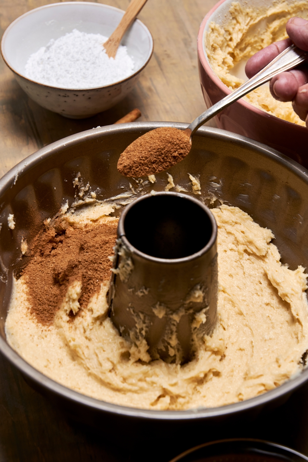 A bundt pan with half the cake batter being topped with cinnamon and sugar.