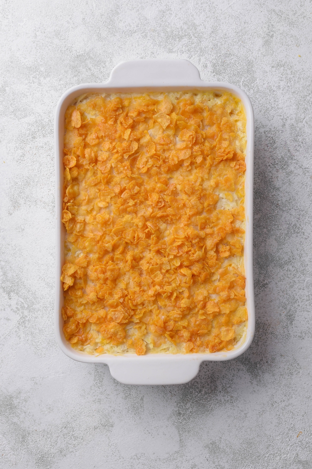 A casserole dish with baked hash brown casserole topped with corn flakes.