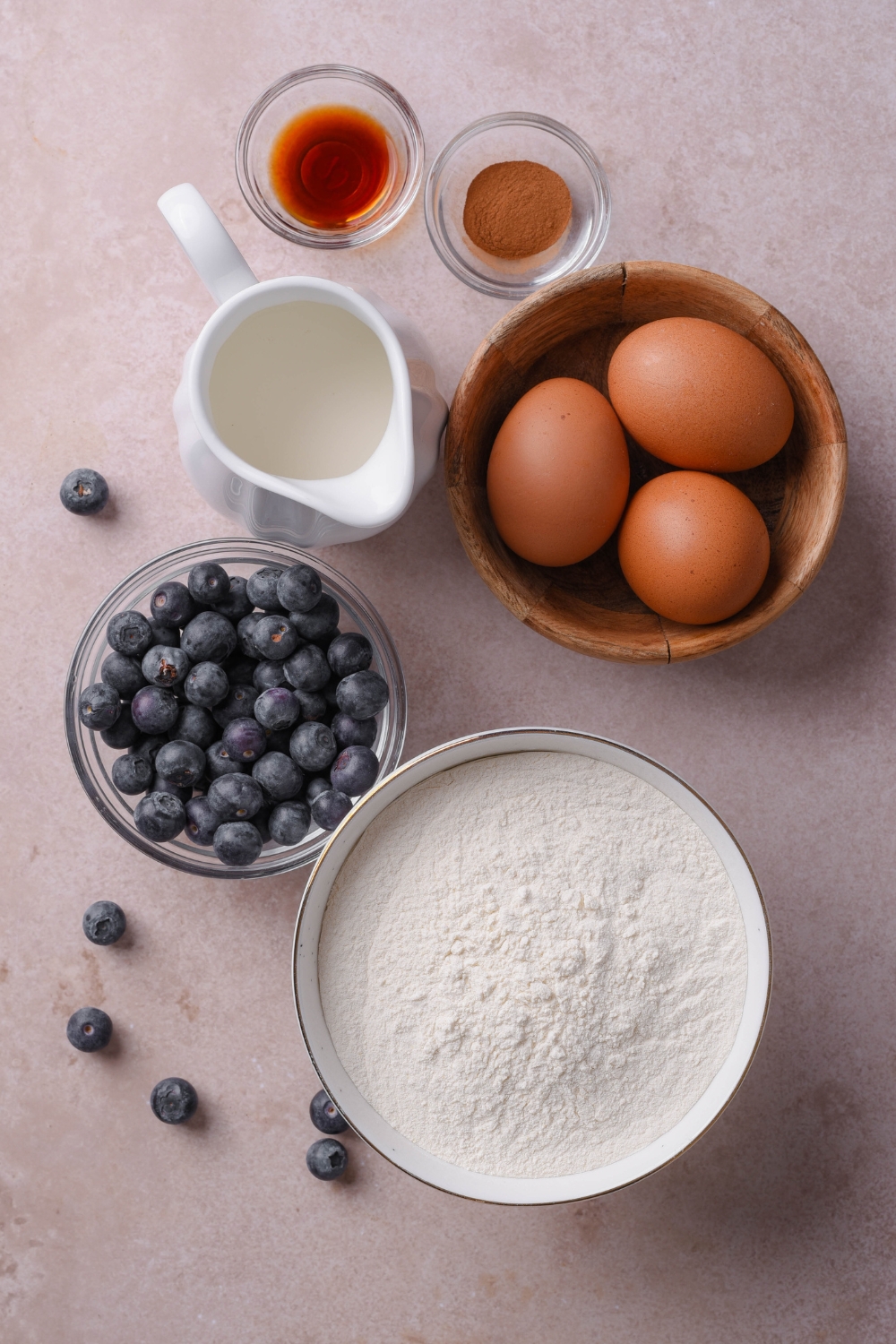 A countertop with eggs, vanilla, cinnamon, milk, blueberries, and pancake mix in separate bowls.