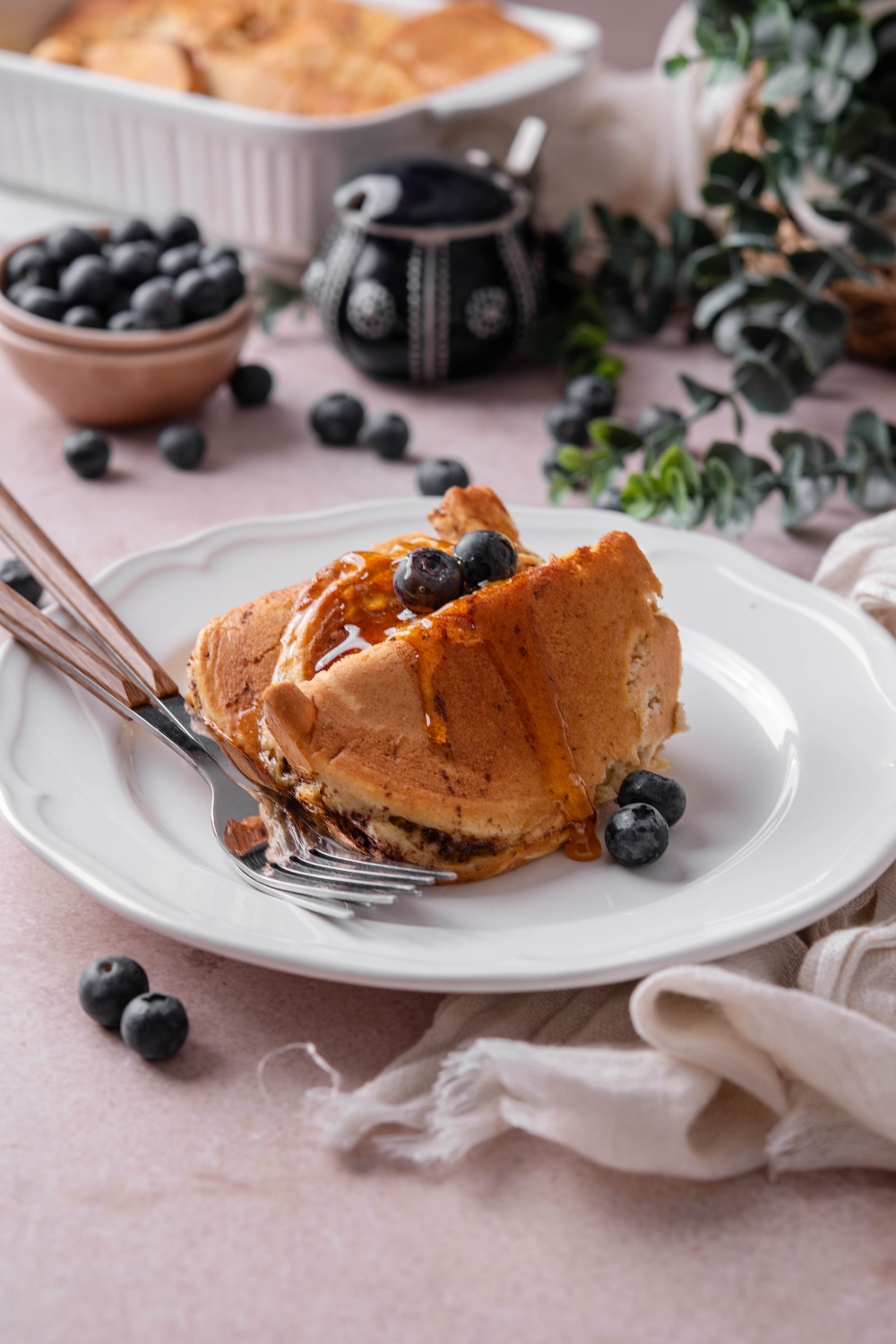 A plate with pancake casserole topped with blueberries and maple syrup.