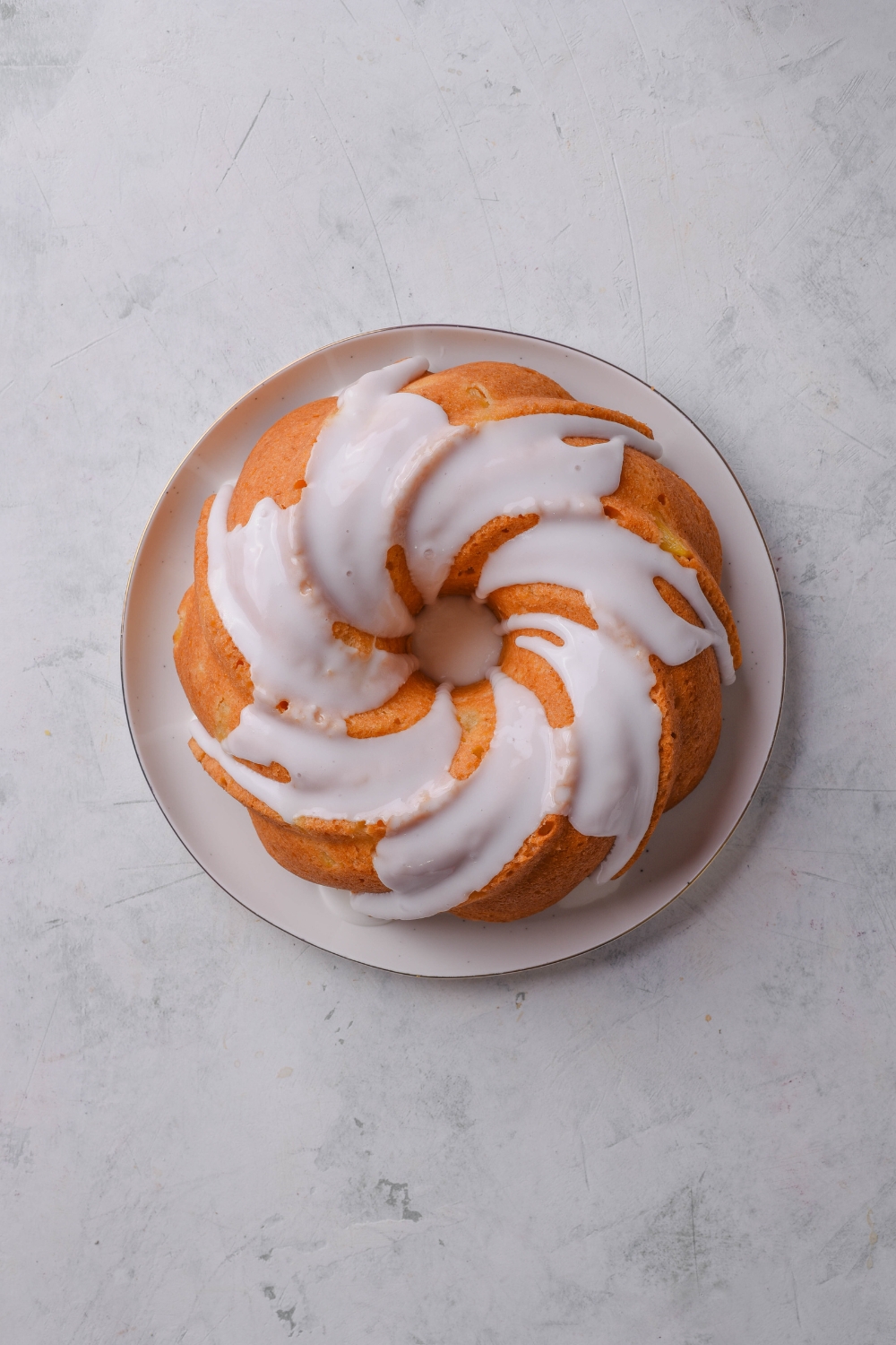 An iced golden brown loaf of pineapple pound cake is on a white serving platter.