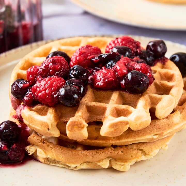 Three waffles on top of one another on a plate with berries on top.