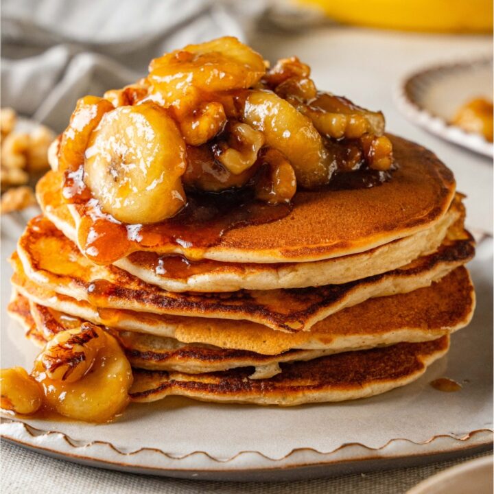 A stack of bananas foster pancakes topped with caramelized banana slices.