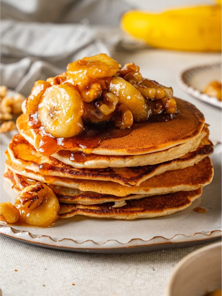 A stack of bananas foster pancakes topped with caramelized banana slices.
