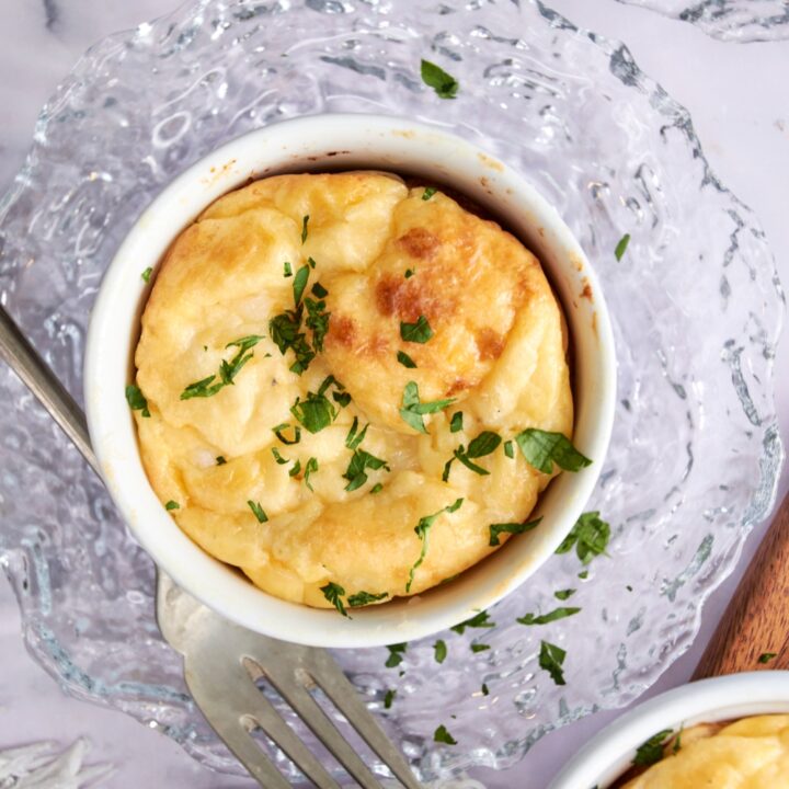 A white ramekin filled with Panera souffle sits on a glass plate. A fork rests on the plate next to the souffle.