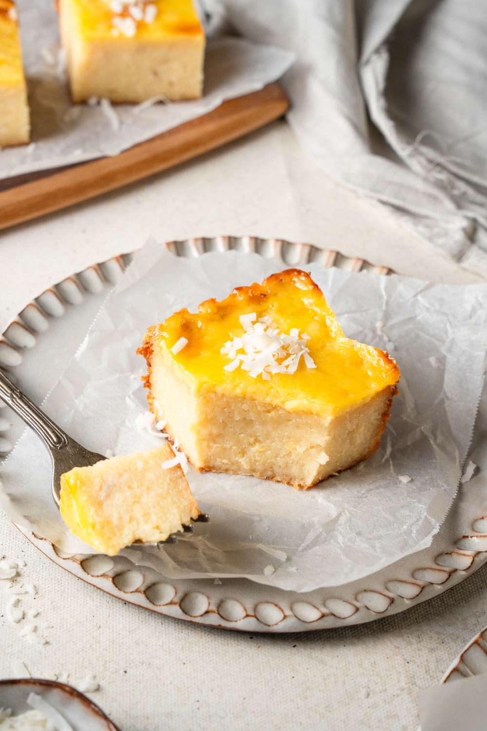 A bite of cassava cake is resting on a fork. The fork sits on a plate holding another piece of cassava cake.