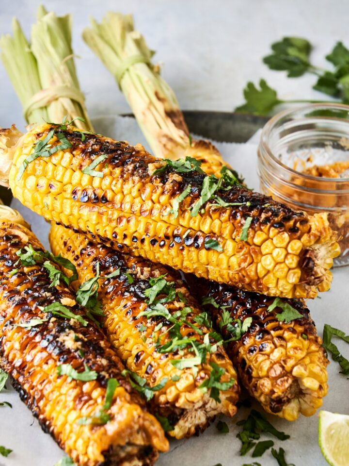 Four ears of corn are on a serving plate. They have been garnished with fresh chopped cilantro.
