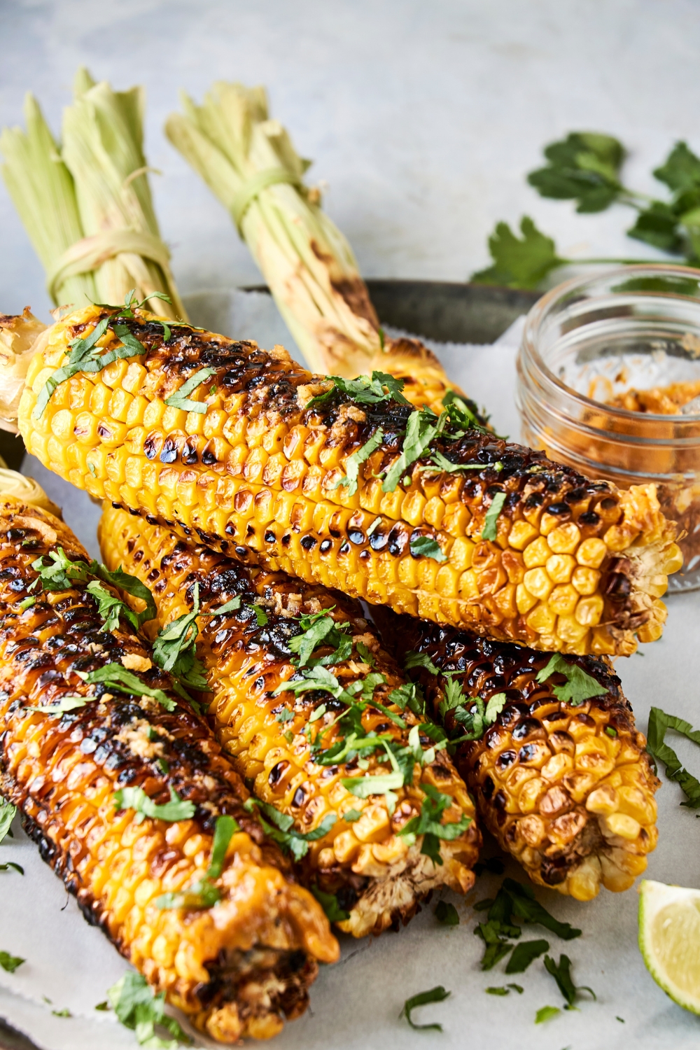 Four ears of corn are on a serving plate. They have been garnished with fresh chopped cilantro.