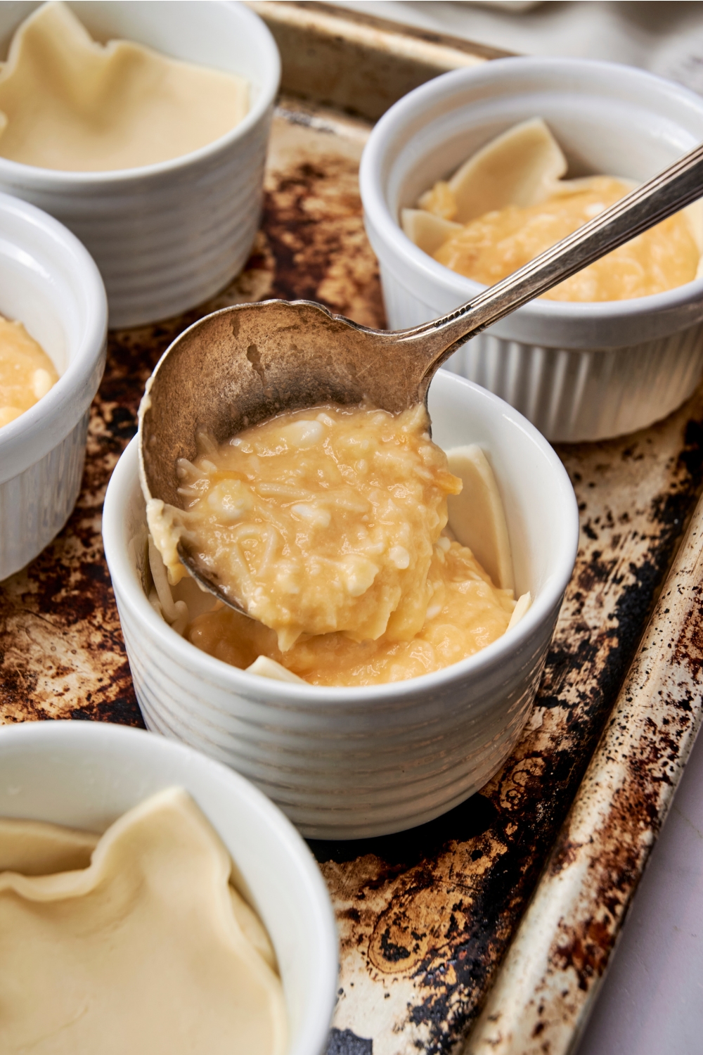 Someone spoons egg and cheese mixture in a ramekin lined with puff pastry.