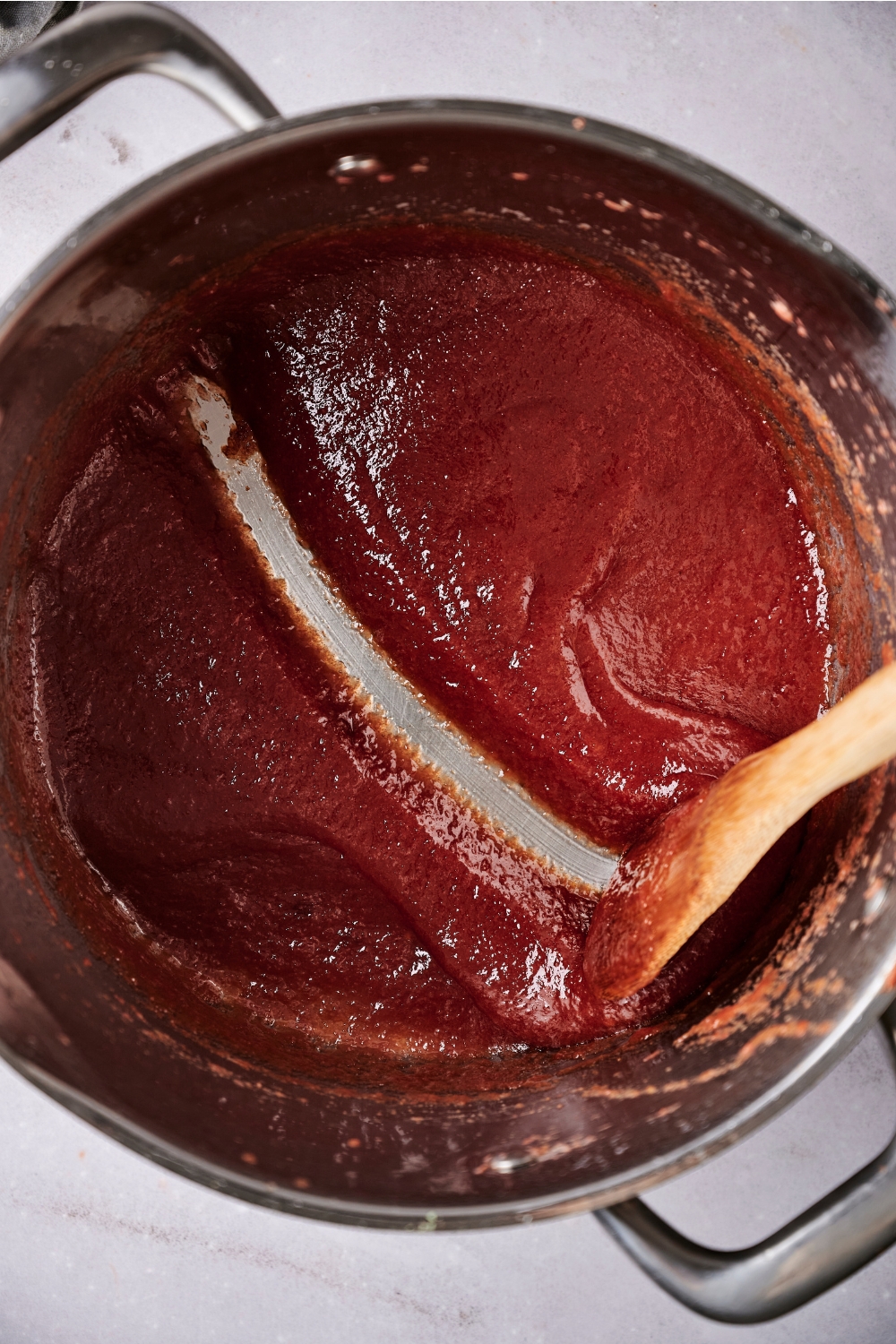 Reduced guava paste is in a large silver pot. Someone has drawn a line in the paste using a wooden spatula.