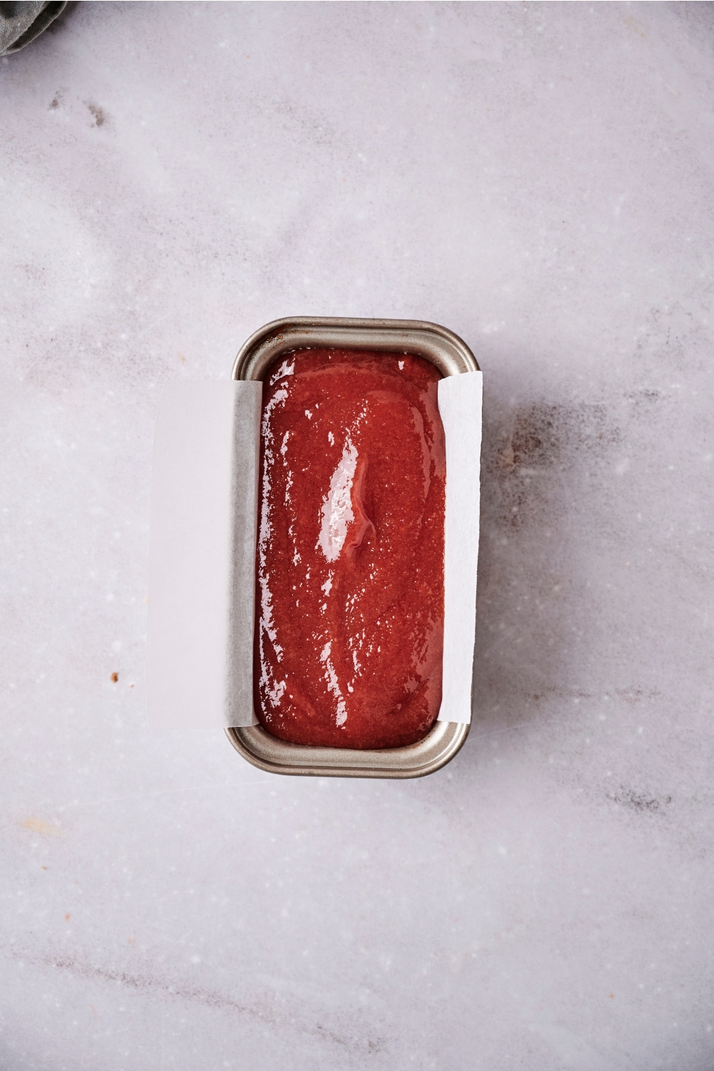 A small loaf pan is lined with parchment paper. The guava paste has filled the loaf pan to the top.