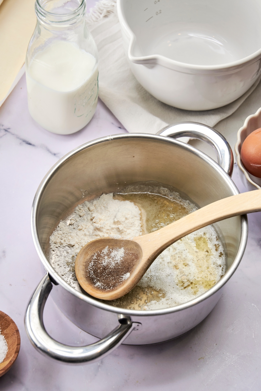 A silver pot holds melted butter and flour. A wooden spoon rests in the pot, also.