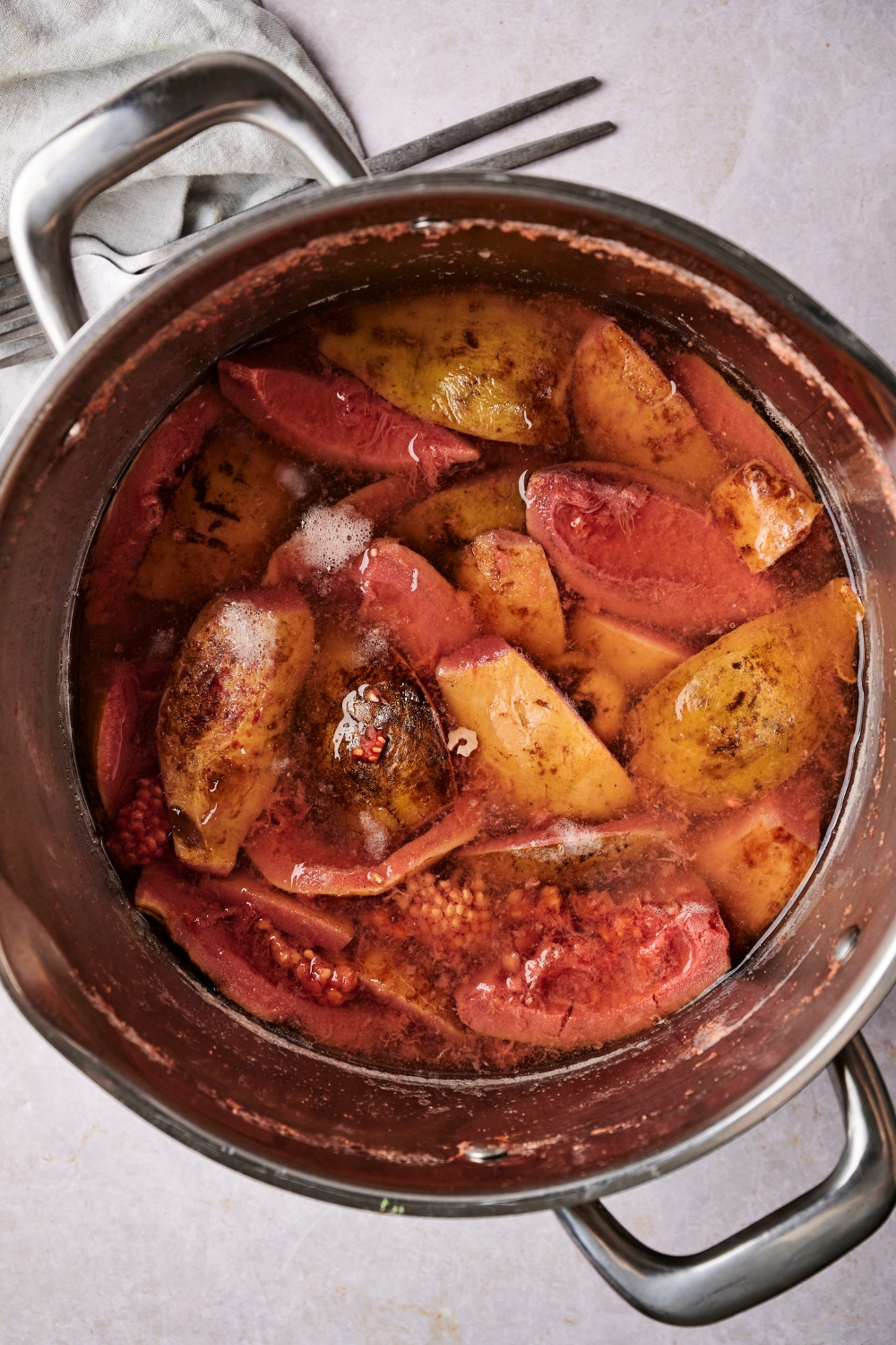 A large silver pot is full of water and pieces of guava.