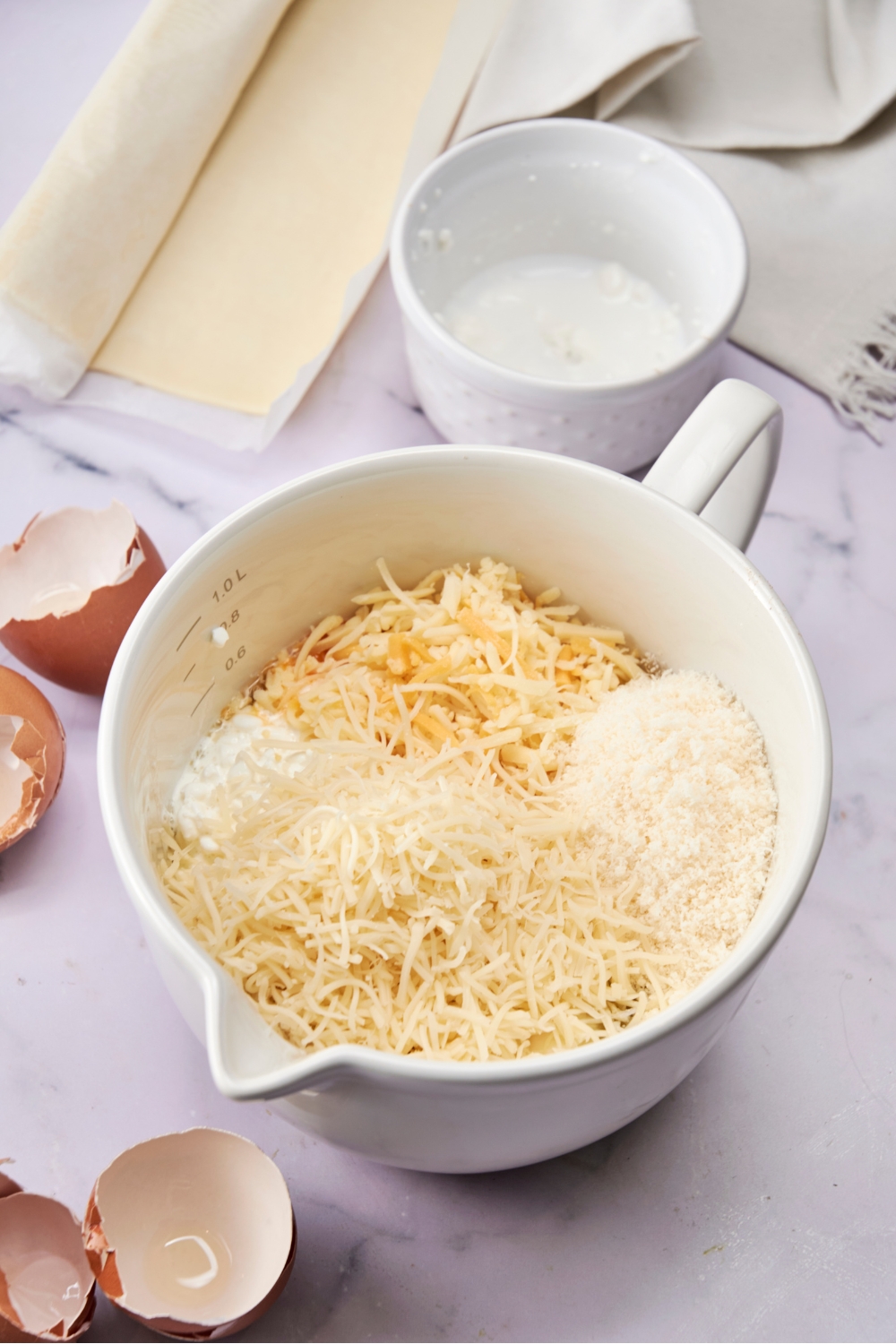 A large white mixing bowl is full of egg mixture and cheeses.