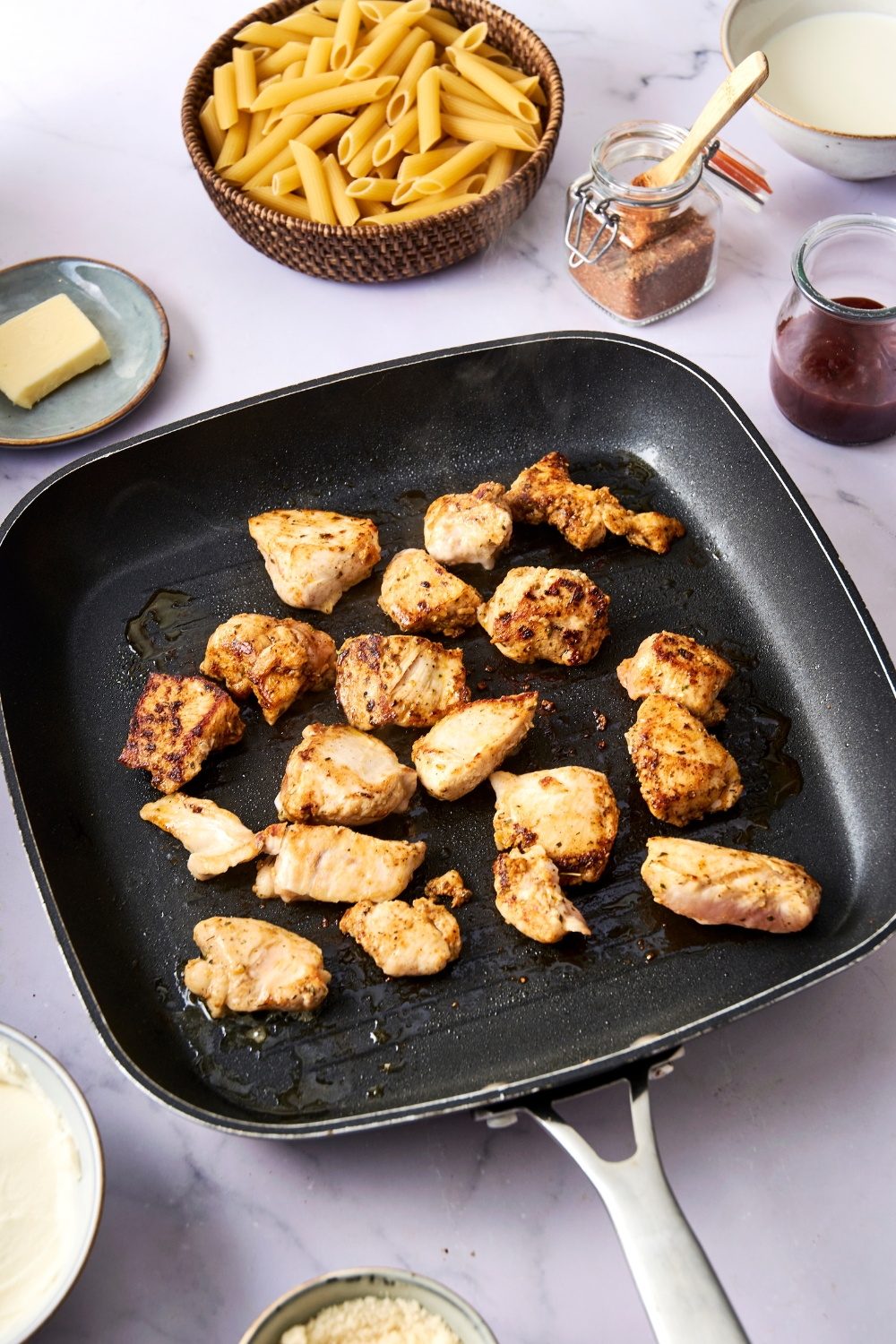 A square grill pan is full of diced and seasoned chicken breast.