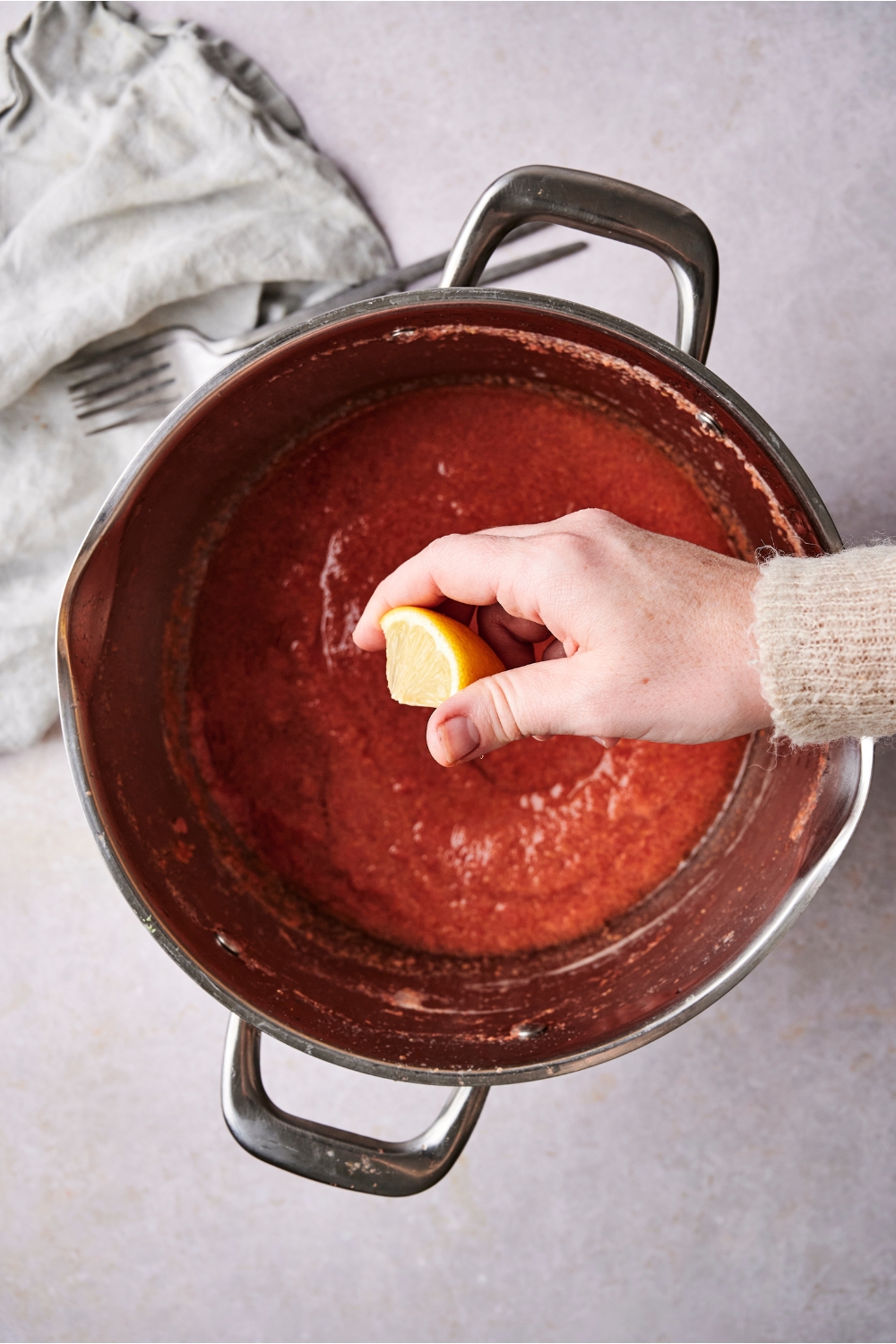 Someone squeezes a wedge of lemon into a large pot filled with guava puree.