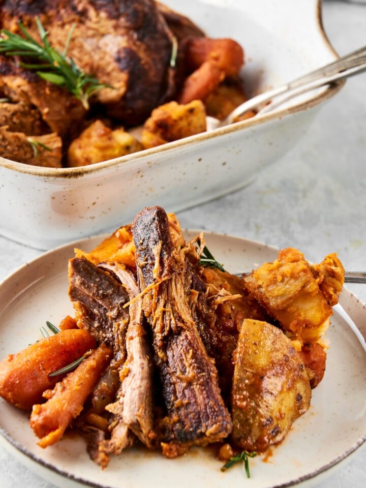 A white dish is piled high with crock pot chuck roast and vegetables.