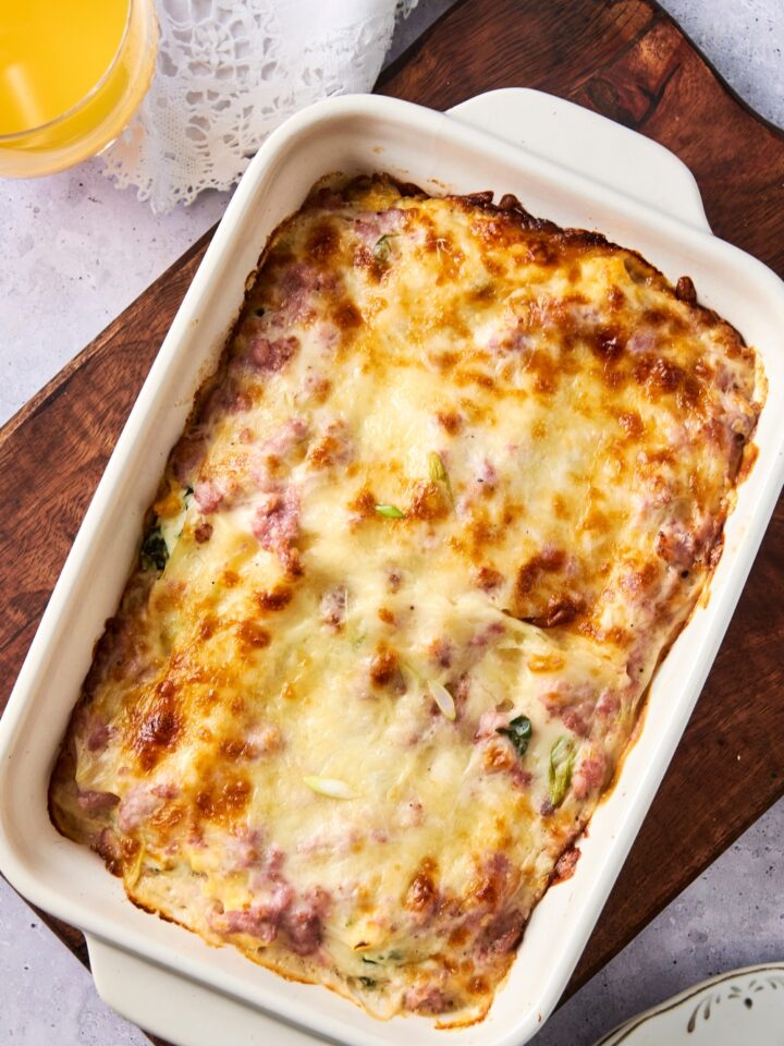 A white casserole dish is full of breakfast lasagna. The top layer of cheese is beautifully golden brown and melted.