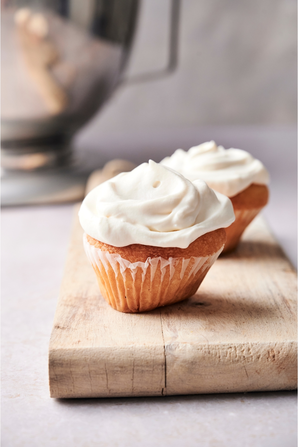 Two cupcakes with creme fraiche frosting sitting on a wooden board.