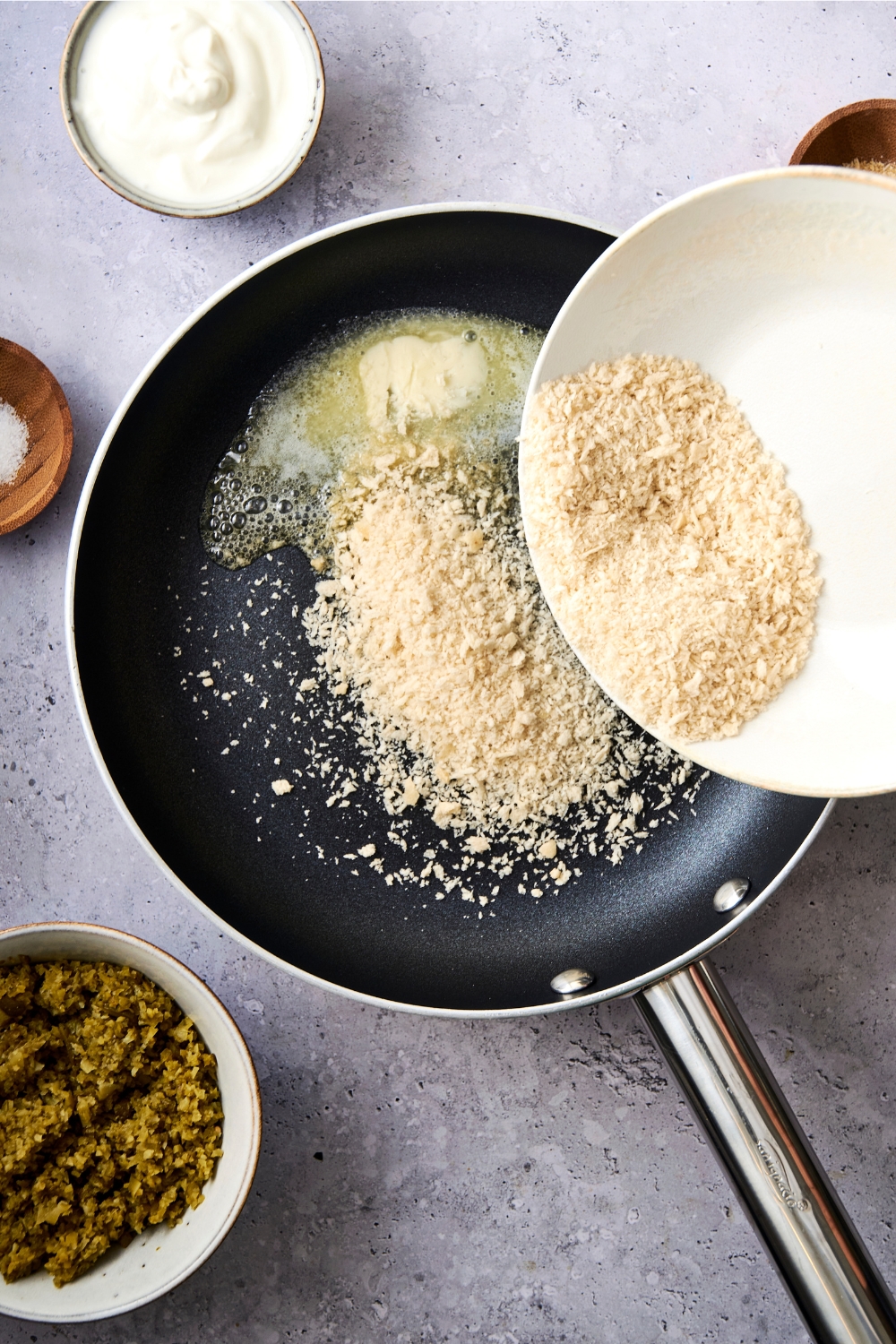 A frying pan with melted butter and panko bread crumbs being added to it.