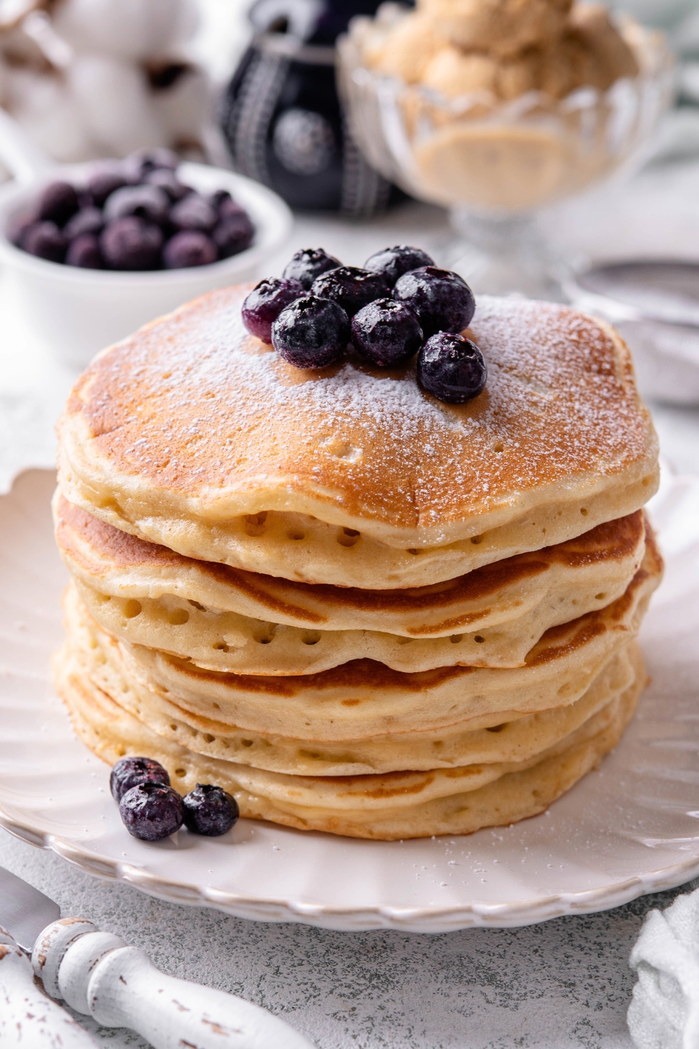 A stack of six pancakes with blueberries on top on a white plate.