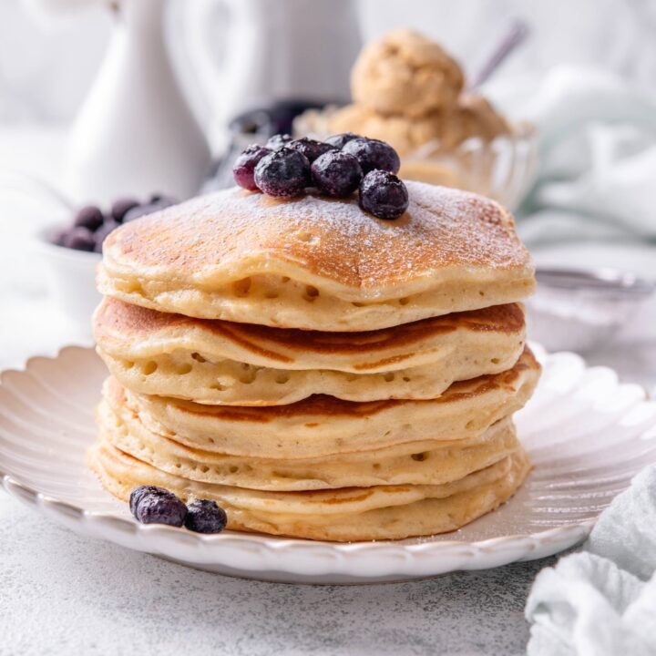 A stack of six pancakes on a white plate.