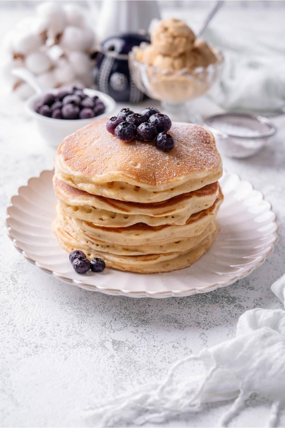 A stack of six pancakes on a white plate with blueberries on top.