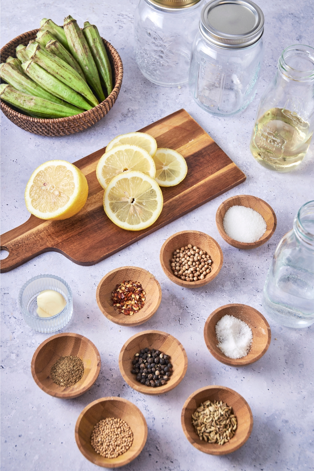 A countertop with a wooden cutting board with sliced lemons, small bowls with the pickling spices, water, and cut okra.