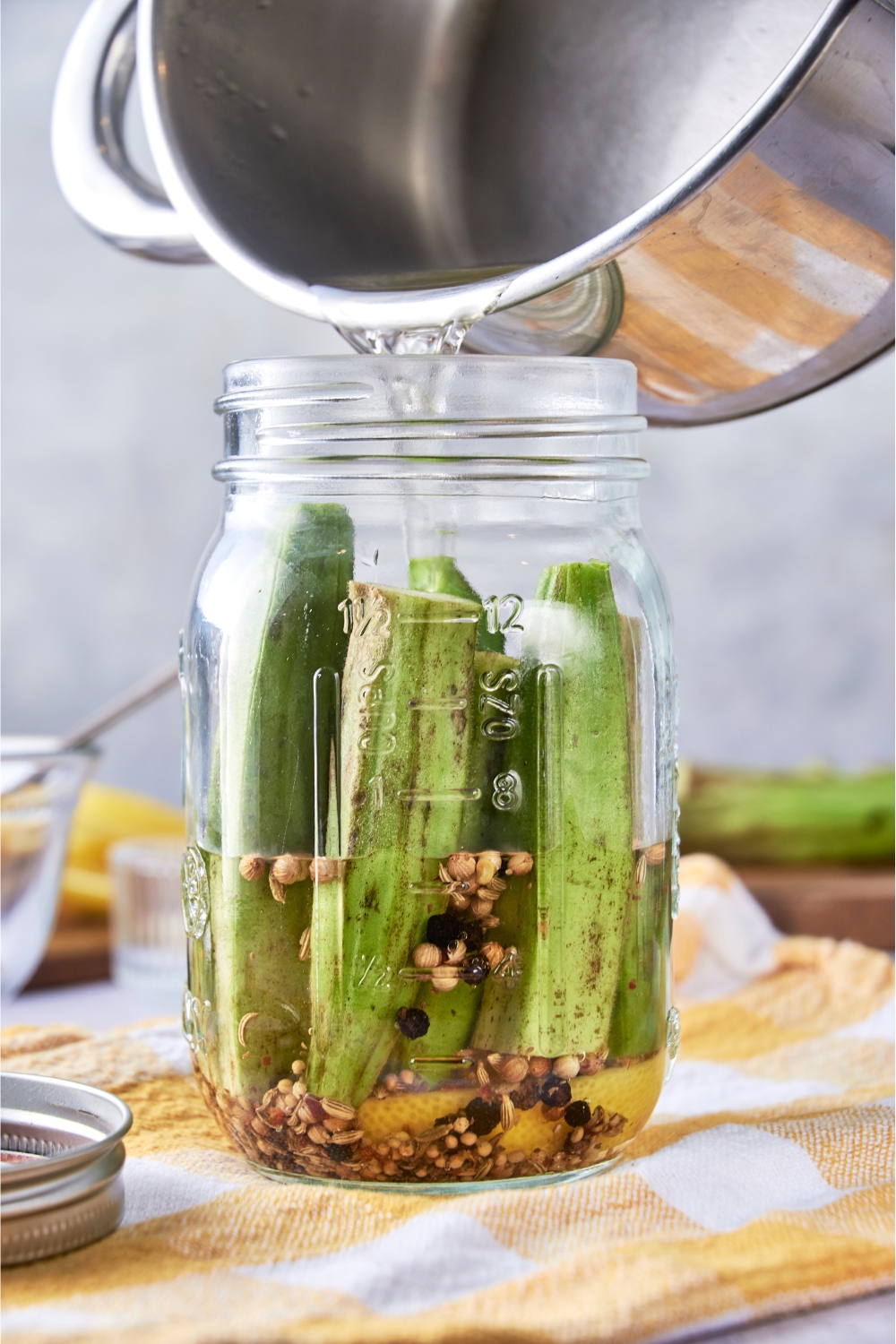 A pot pouring brine into the jar with the okra.