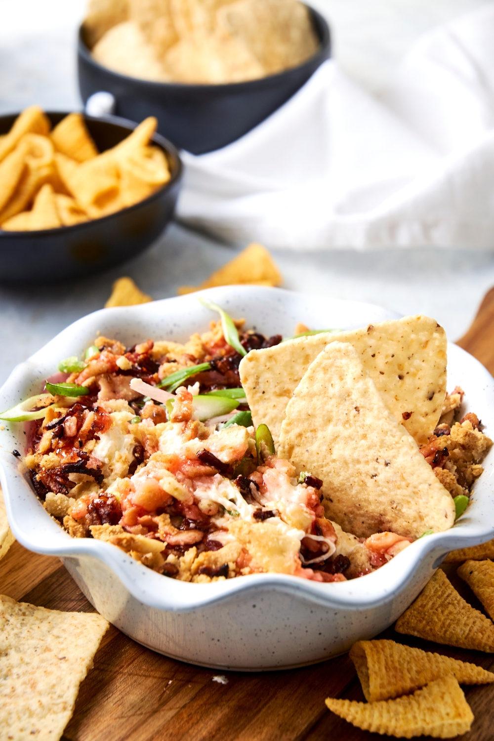 A serving bowl with captain rodney's dip garnished with captain rodney's pepper sauce and chopped green onion. With tortilla chips in it.