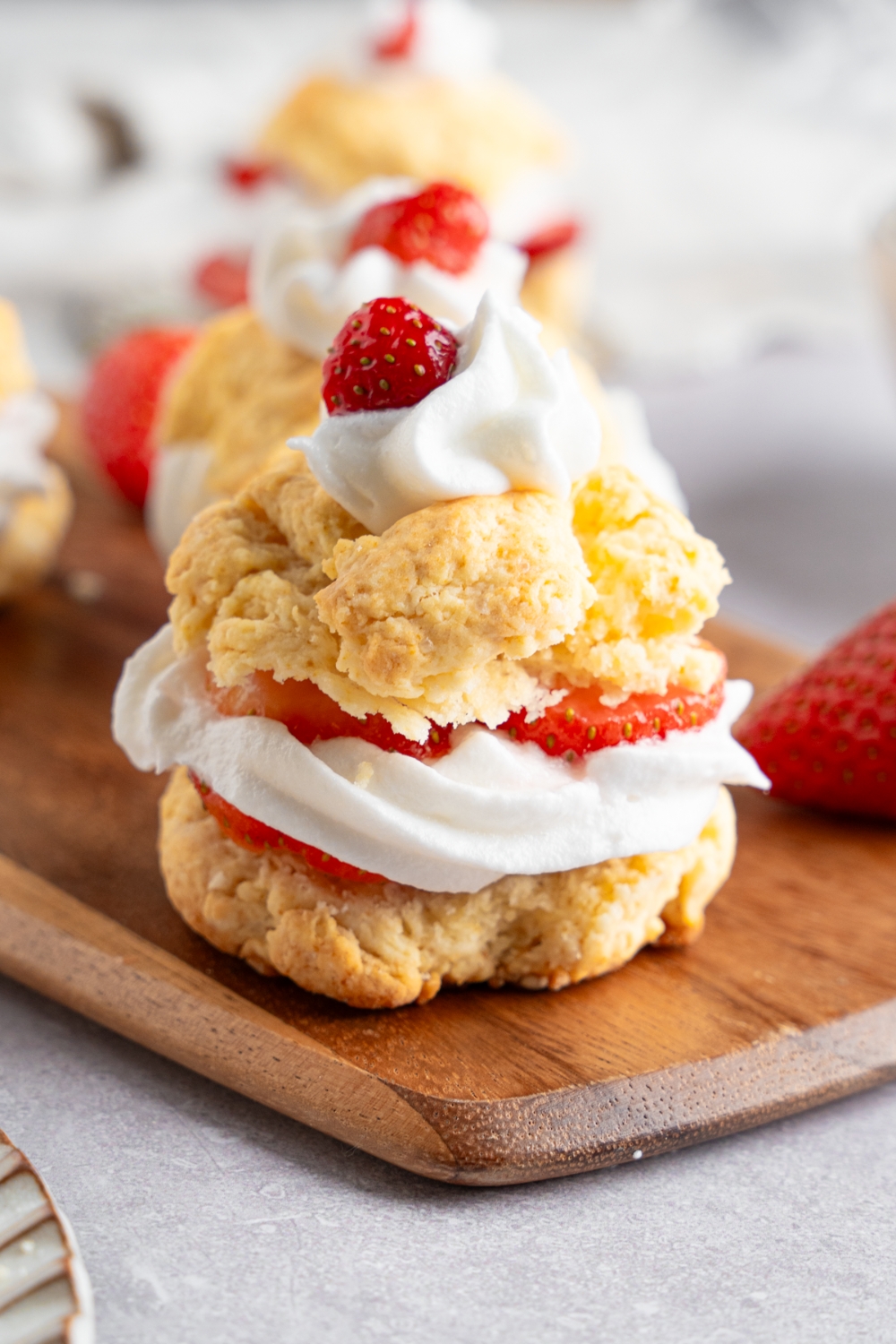 A Bisquick strawberry shortcake made with sliced shortcake layered with strawberries and whipped cream. The shortcake is on a wooden serving board with additional shortcakes and strawberries. The board is on a white counter.
