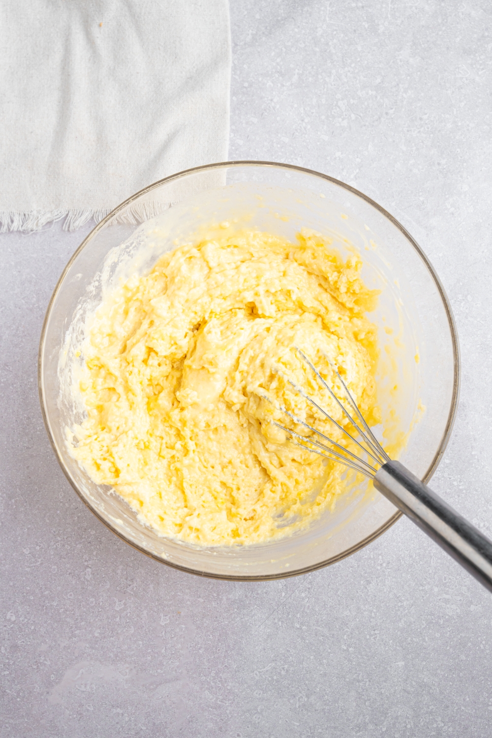A glass bowl with a whisk mixing Bisquick dough. The bowl is on a white counter with a white napkin.