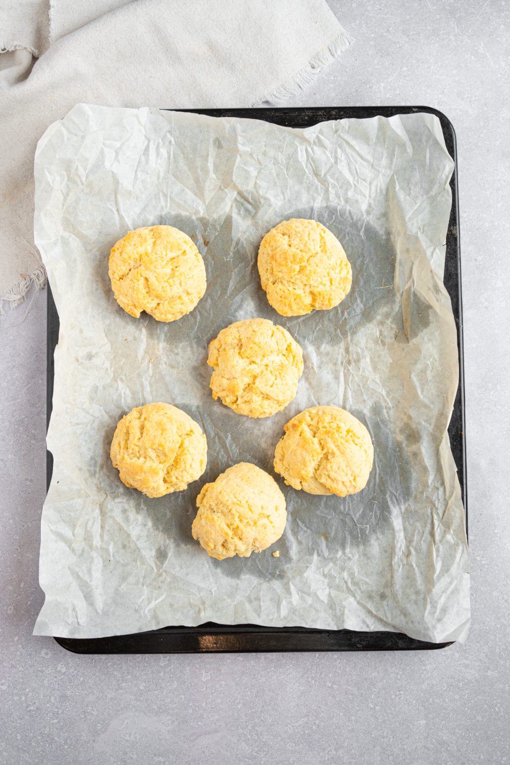 A baking sheet lined with parchment paper with 6 baked Bisquick shortcakes. The sheet is on a white counter with a white striped napkin.