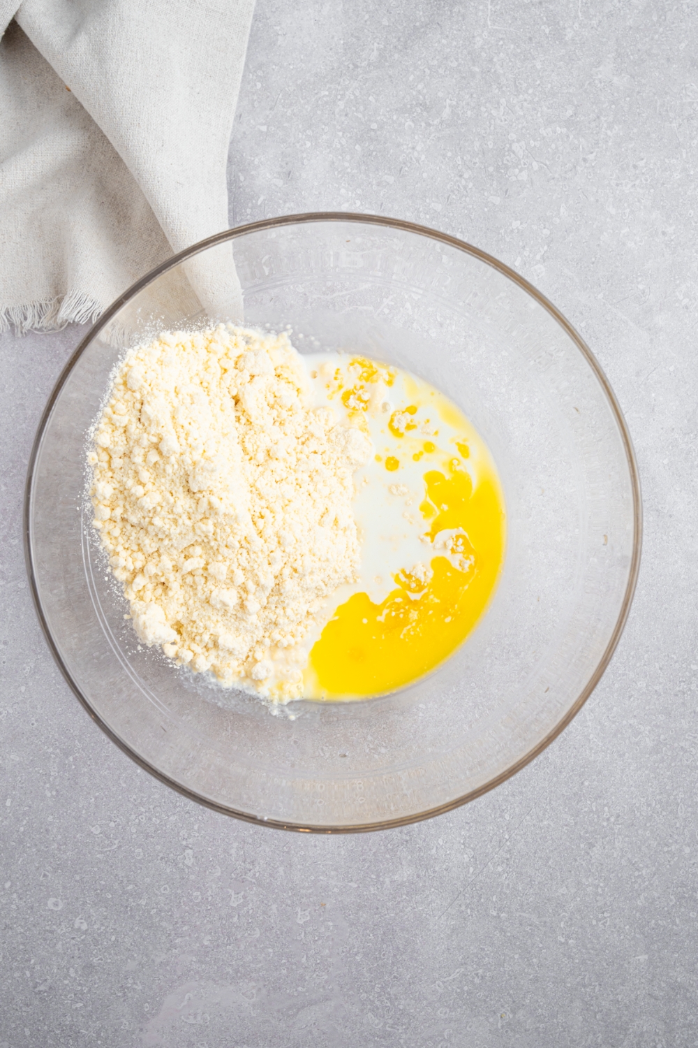 A glass bowl with ingredients to make Bisquick shortcakes including Bisquick baking mix, melted butter, and milk. The bowl is on a white counter with a white cloth napkin.