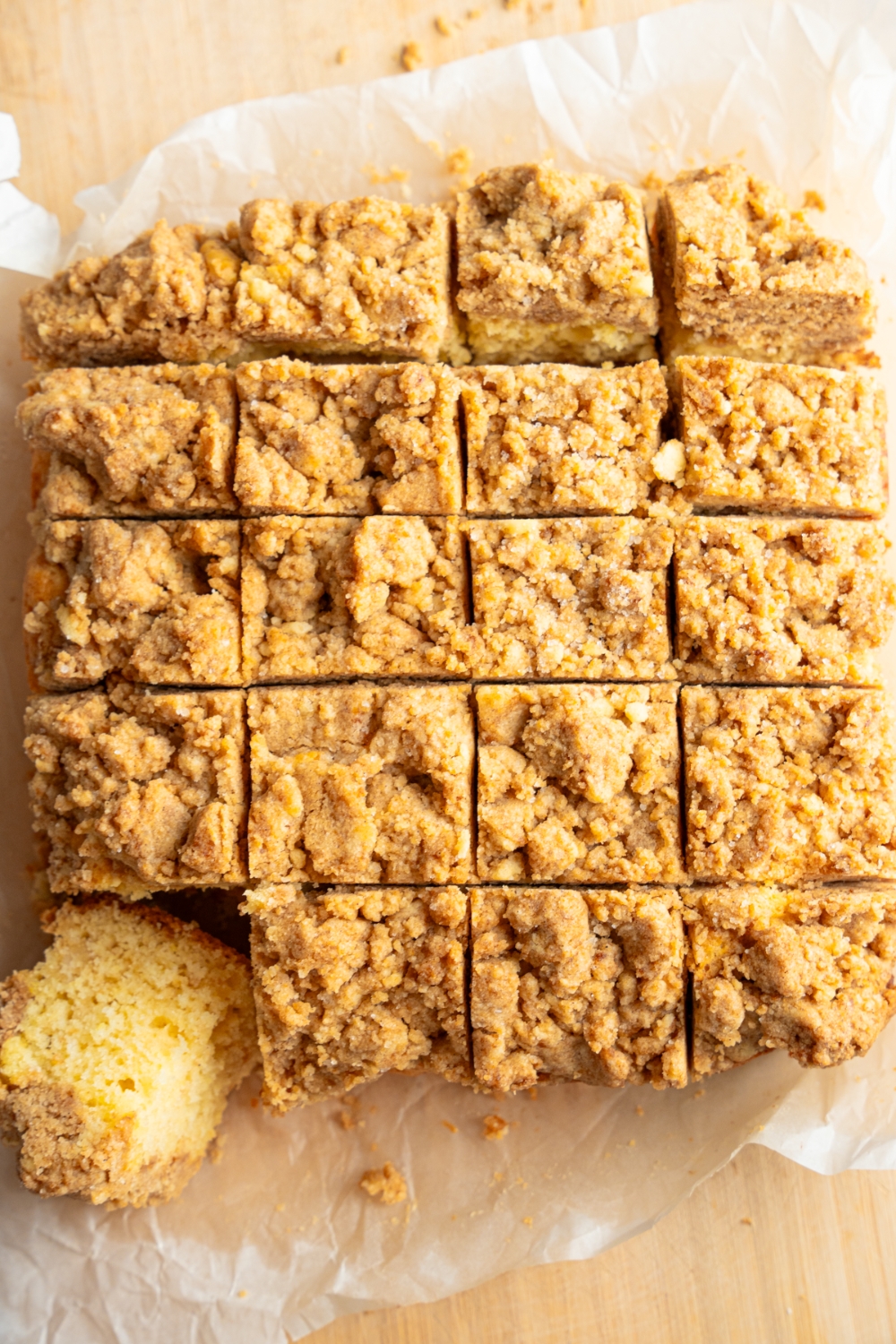 A whole Bisquick coffee cake sliced in squares on a piece of parchment paper over a wooden board. One slice is tipped out of the cake.