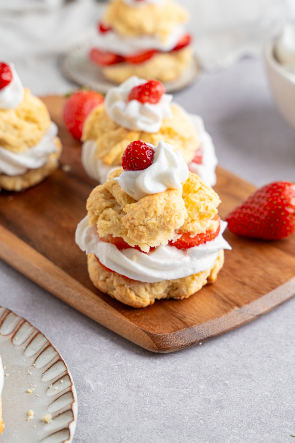 A Bisquick strawberry shortcake made with sliced shortcake layered with strawberries and whipped cream. The shortcake is on a wooden serving board with additional shortcakes and strawberries. The board is on a white counter.