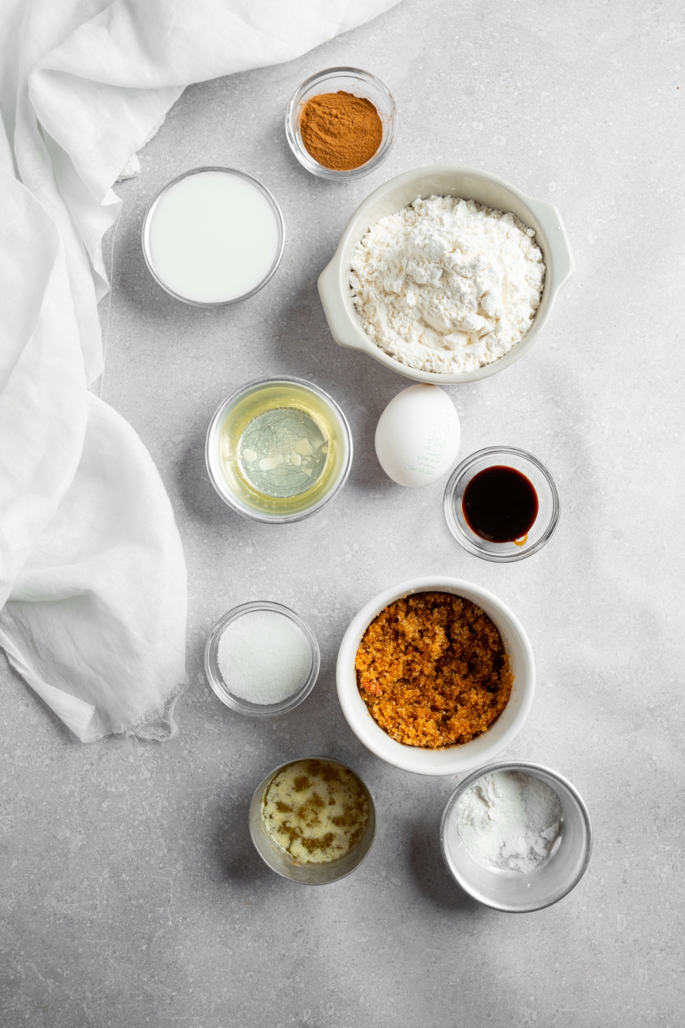 An overhead shot of several bowls in various sizes containing ingredients to make coffee cake muffins including flour, cinnamon, baking powder, baking soda, brown sugar, oil, egg, vanilla, sugar, and butter.