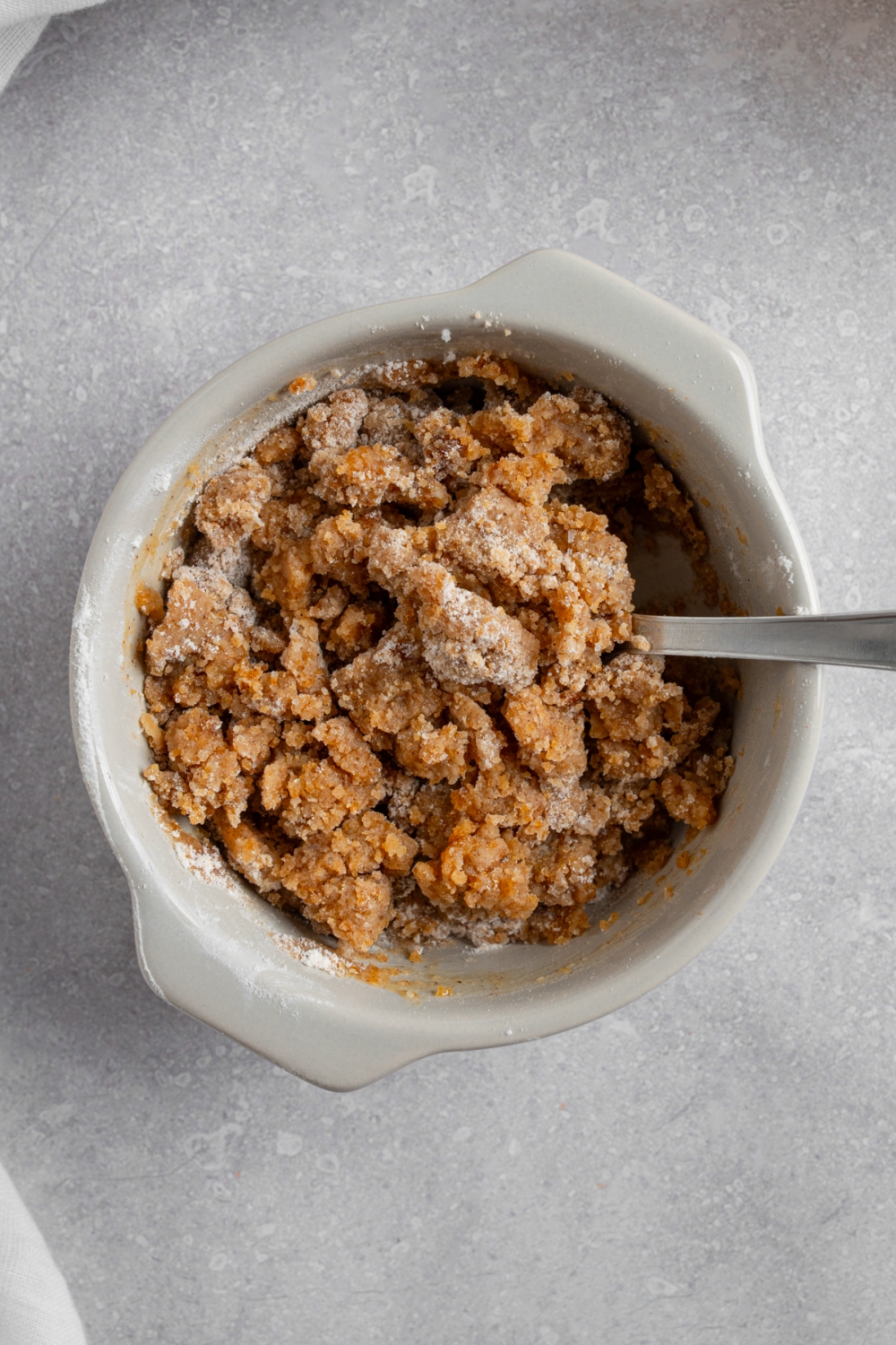 A small ceramic bowl with a spoon combining ingredients to make a coffee cake crumble topping.