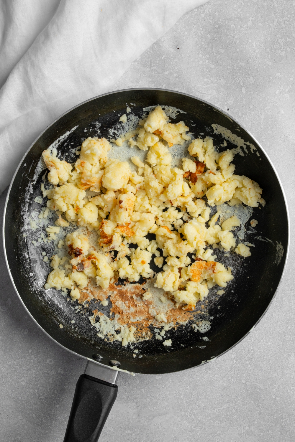 A skillet with cooked scrambled pancakes. The skillet is on a white counter with a white cloth napkin.