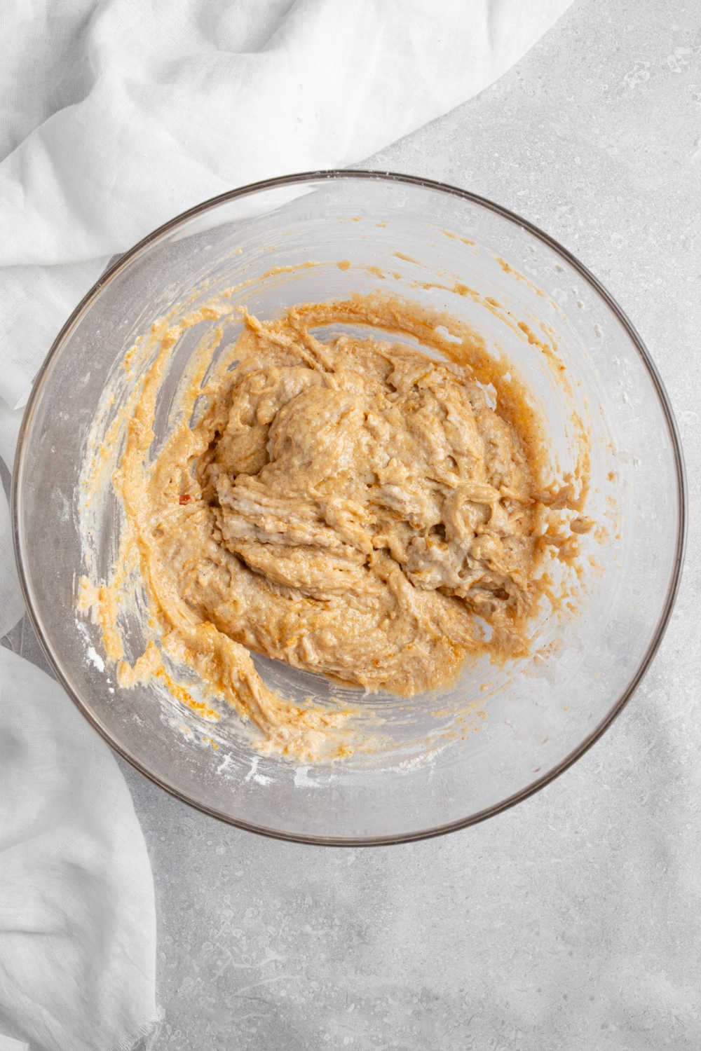 A glass bowl with coffee cake muffin batter. The bowl is on a white counter with a white cloth napkin.