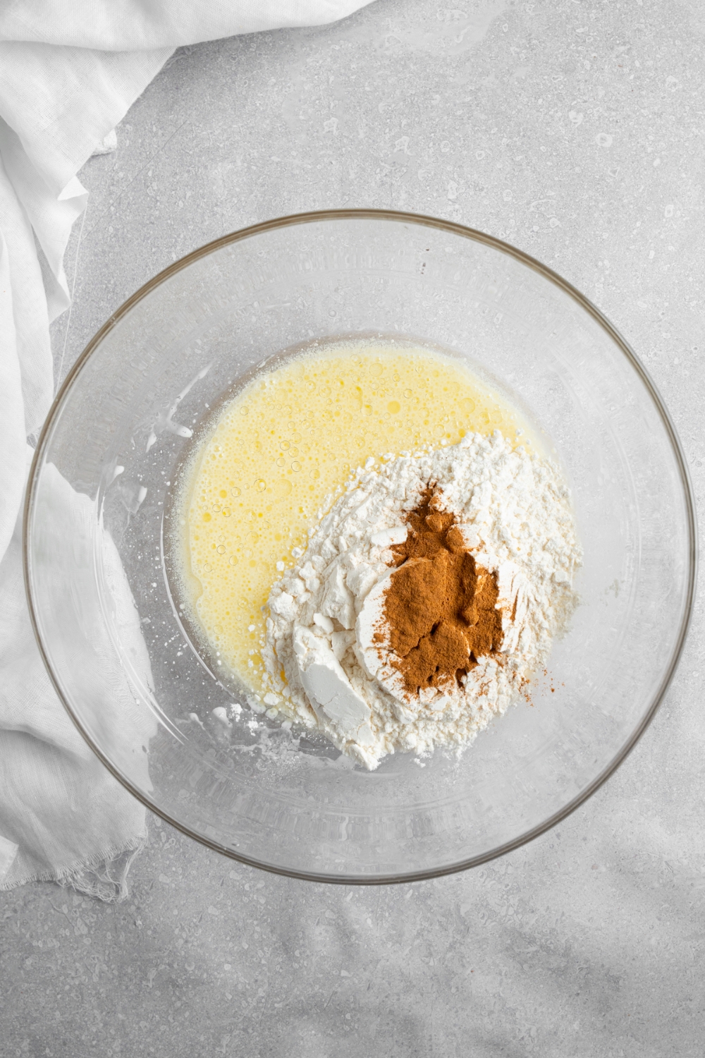 A glass bowl with ingredients to make coffee cake muffin batter. The bowl is on a white counter with a white cloth napkin.