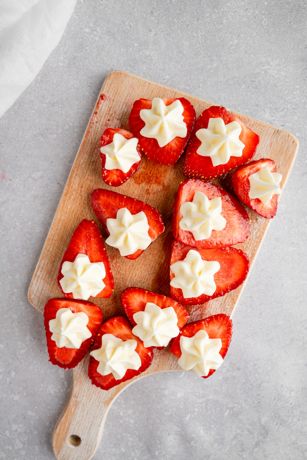 A wooden board with sliced strawberries topped with piped cream cheese filling. The board is on a white counter with a white cloth napkin.