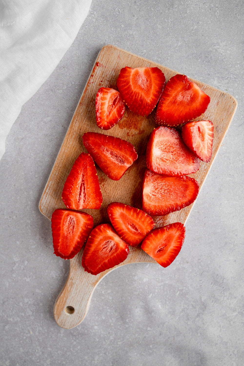 A wooden board with sliced strawberries. The board is on a white counter with a white cloth napkin.