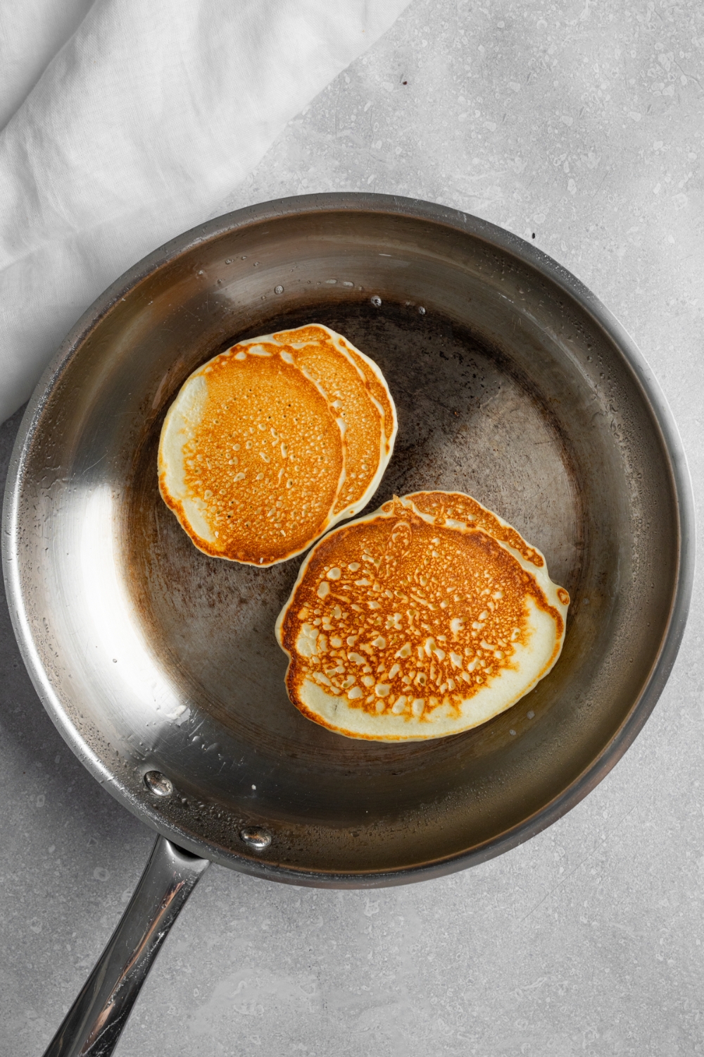 A skillet with two pancakes. The skillet is on a white counter.