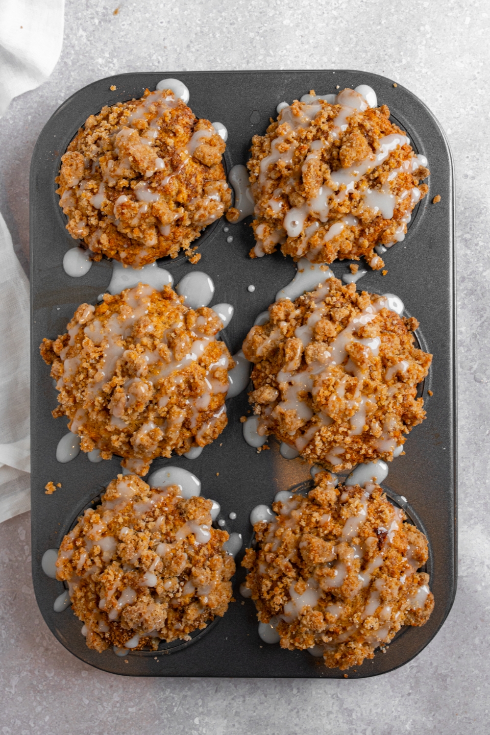 A muffin tin with baked coffee cake muffins drizzled with vanilla glaze.