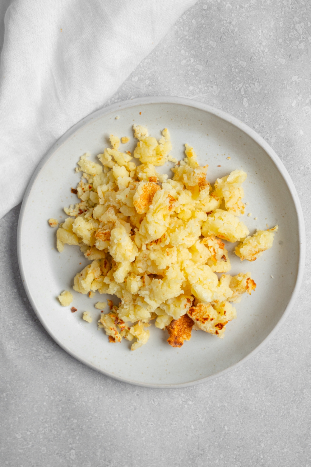 A white plate with scrambled pancakes. The plate is on a white counter with a white cloth napkin.