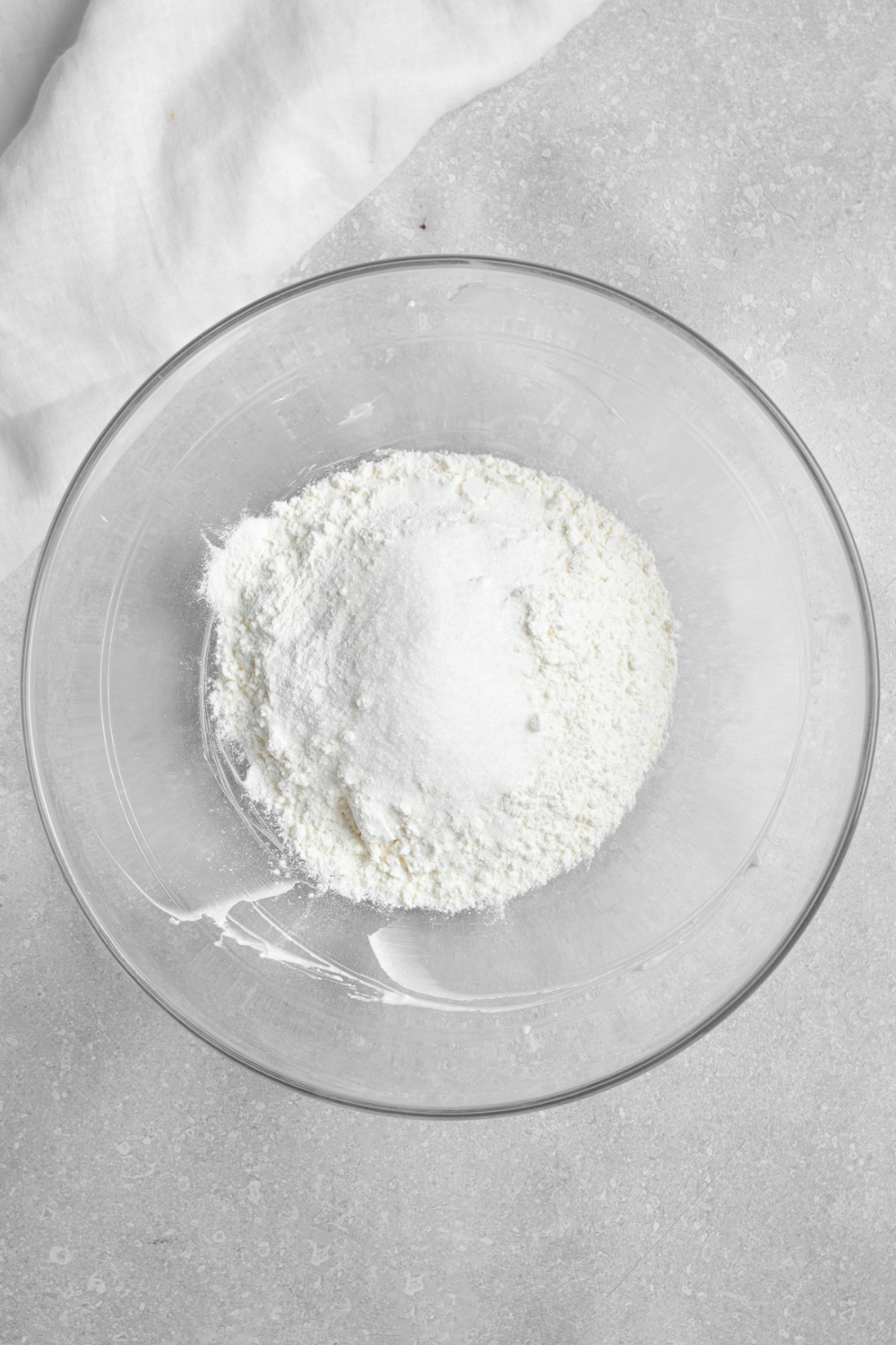 A glass bowl with dry ingredients for pancake batter. The bowl is on a white counter with a white cloth napkin.